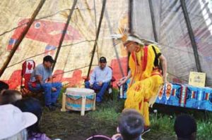 PHOTO BY TIM KALINOWSKI- Ben Lloyd demonstrates a "Grass Dance" for school kids while drummers, Readford Blackrider (right) and Shawn Redcrow lay down a beat. About 2,000 students visited the Elkwater Rodeo grounds last week to take in the four days of "History of the Hills".