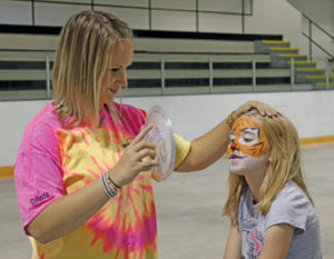 Photo by Jamie Rieger- Dawni Urlacher (left), from McMann Parent Link had a long line of young people waiting to get their faces painted after she was finished painting a tiger face on seven-year old Abigail Bailey.